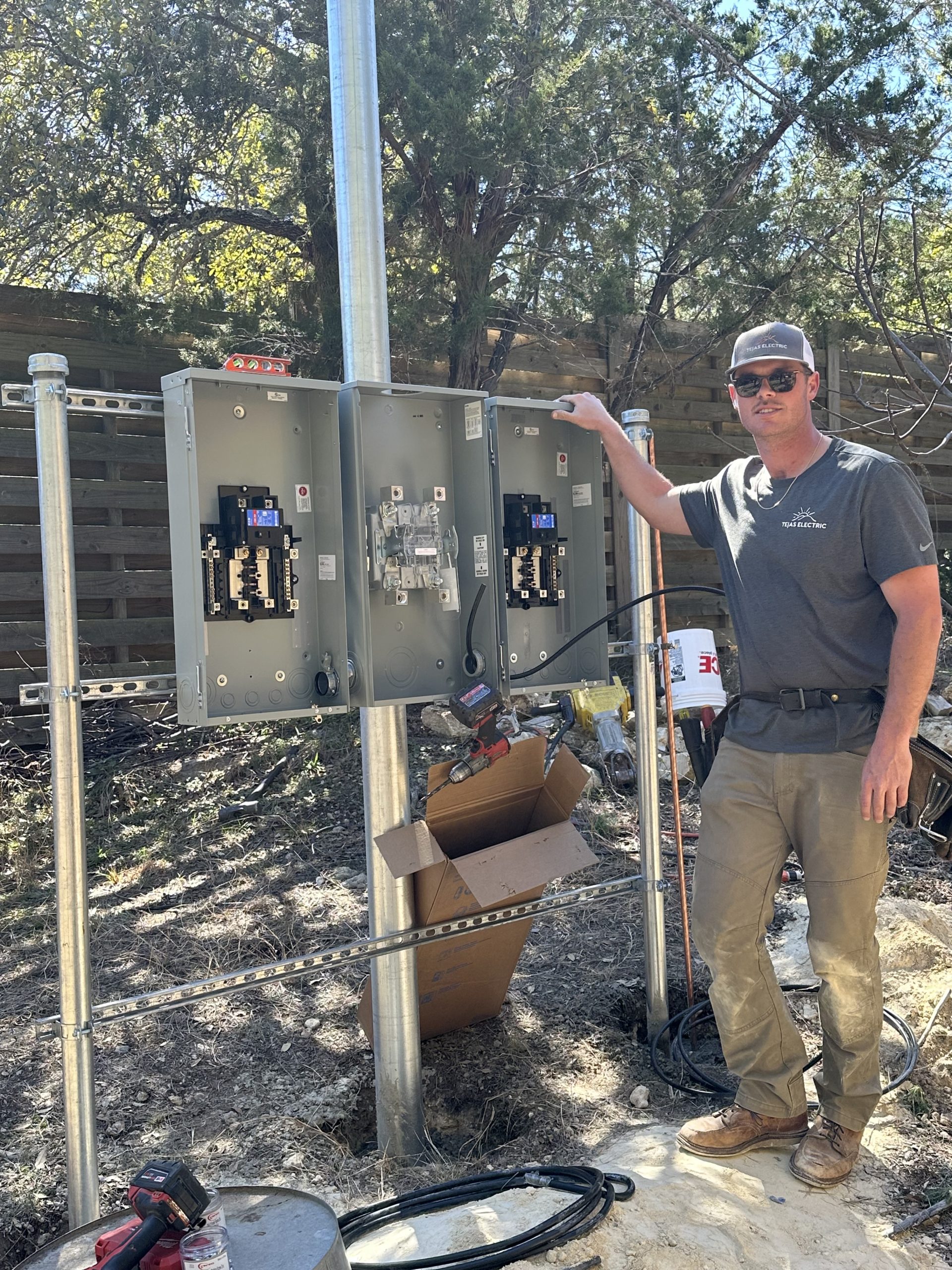 A licensed electrician from Tejas Electric in Spicewood, TX, stands by a newly installed outdoor electrical service panel.